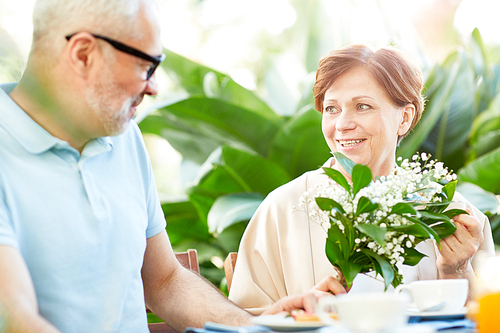 Mature woman with bunch of fresh lilies-of-the-valley talking to her husband by breakfast in home garden