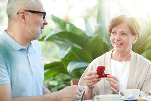 Mature woman holding red velvet box with diamond ring and saying thanks to her husband while spending time together