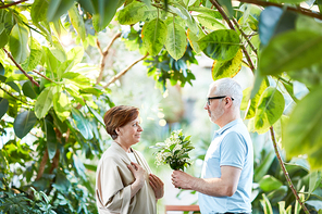 Mature man giving bunch of fresh and aromatic lilies-of-the-valley to his wife while taking walk in the garden