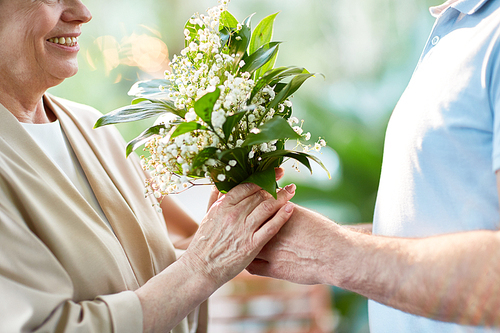Bunch of tender white flowers in hands of senior spouses as symbol of romantic love