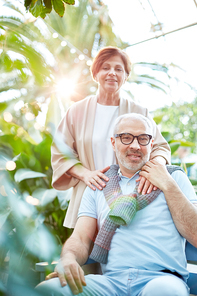 Happy mature man in blue casualwear and his wife  in natural environment among green plants