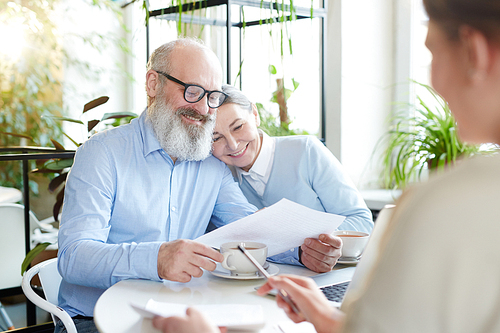 Mature man and woman reading points and terms of contract or agreement during meeting with agent in cafe