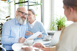 Mature man with paper looking at young agent with his wife sitting close to him