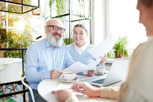 Senior couple with papers having talk with insurance or real estate agent in cafe