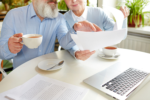 Negotiation of two mature employees with financial documents during tea break in cafe