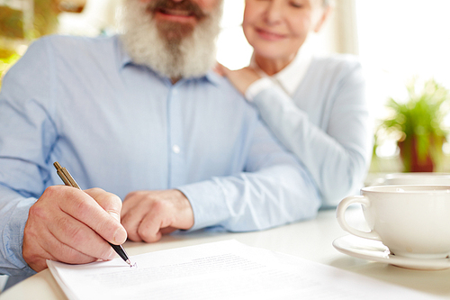 Senior man signing insurance agreement with his wife sitting next to him