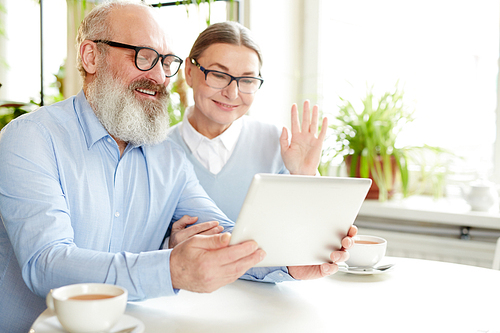 Happy seniors with tablet chatting with their relatives, children or grandchildren through video-chat in cafe