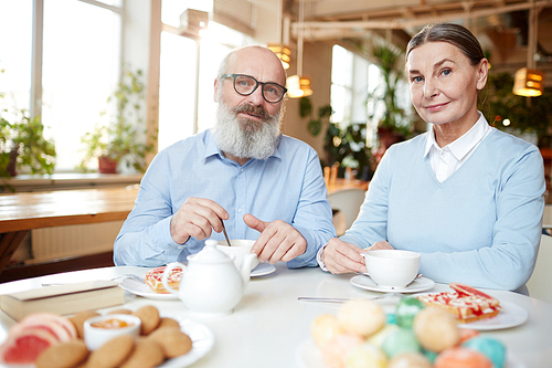 Senior couple sitting by table with cookies and desserts, drinking fresh tea and 