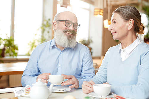 Happy senior man and woman enjoying time and talk in cafe by cup of tea or coffee