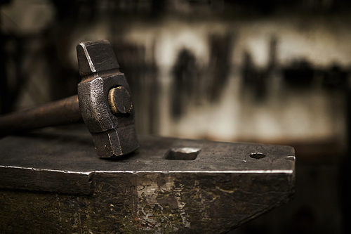 Close-up of heavy hammer placed on durable steel anvil in dark smithery