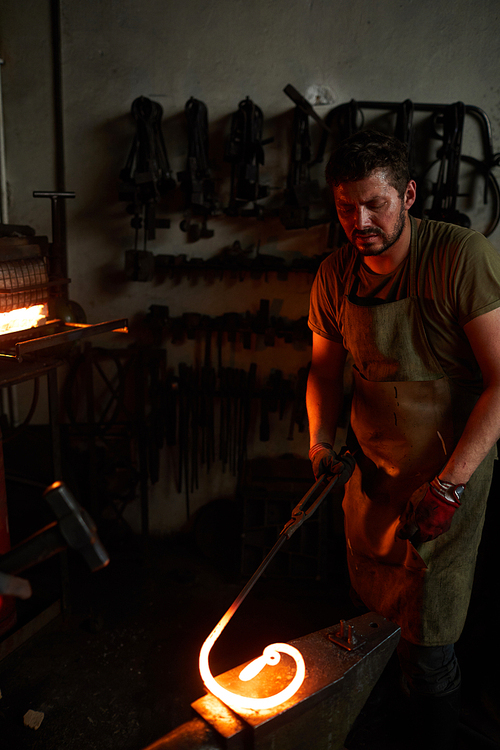 Worker of blacksmith handcraft workshop processing moltem metal workpiece