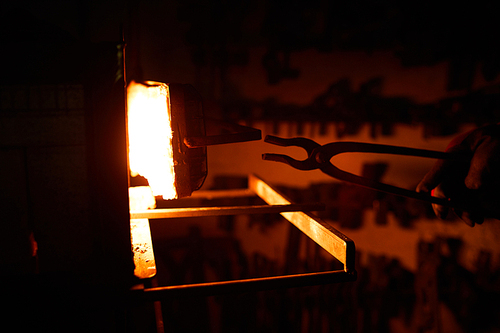 Blacksmith putting iron pincers into hot burning furnace while processing workpiece