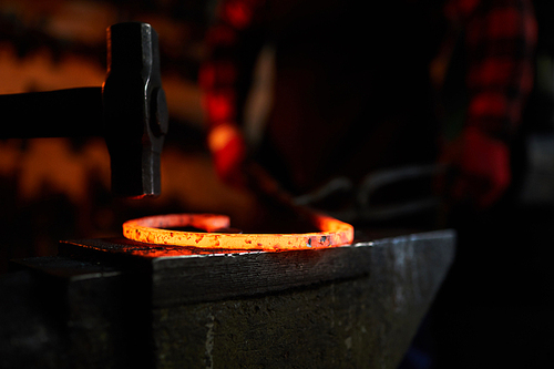 Hammer over hot molten metal workpiece on anvil with blacksmith on background