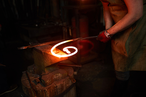 Blacksmith holding hot molten metal spiral workpiece on anvil while working in smithy
