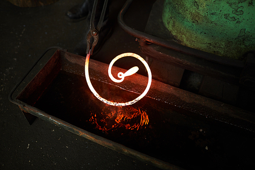 Close-up of blacksmith holding twisted heated metal bar in tongs while cooling it in water
