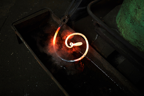 Overview of bent molten metal workpiece in water during blacksmith work process