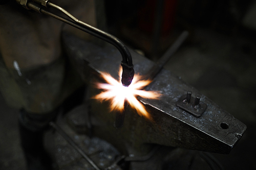 Blacksmith specialist using welding tool while working over iron workpiece on anvil