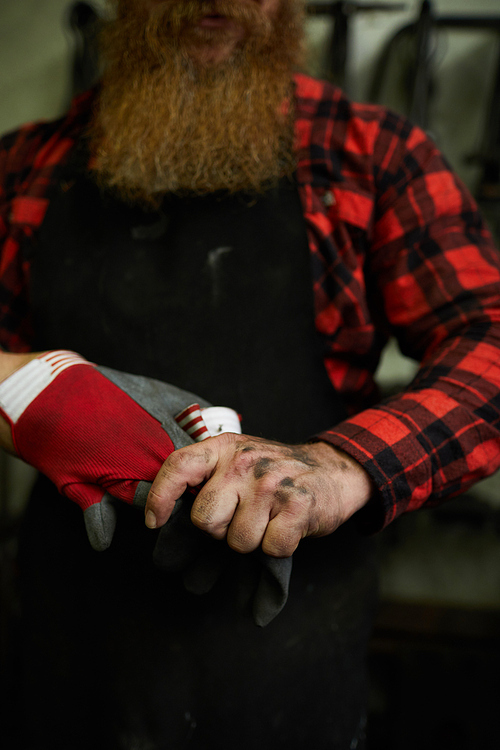 Close-up of unrecognizable male manual worker with dirty hands taking protective gloves off