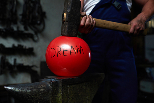 Red inflated ball with note dream situated between anvil and big hammer held by blacksmith