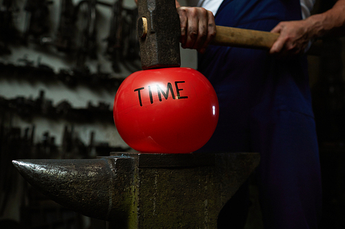 Red ball symbolizing time concept is situated between hammer and anvil