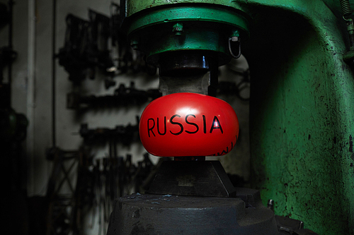 Red inflated ball symbolizing Russia is situated between upper and lower parts of blacksmith machine