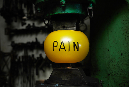 Yellow ball symbolizing pain is situated between two parts of industrial machine