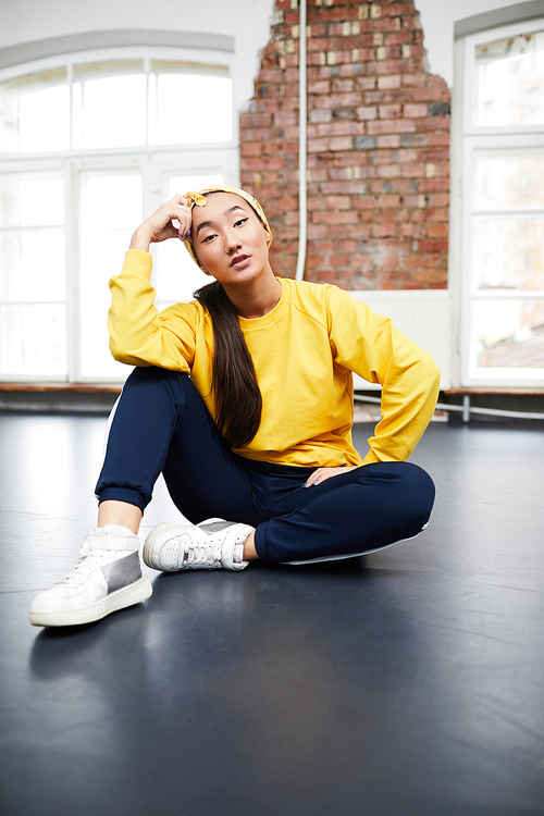 Young woman in activewear sitting on the floor of dance studio after training