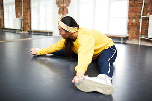 Young active woman doing stretching while sitting on the floor of dance studio