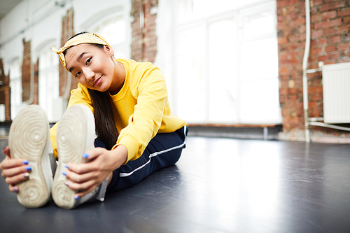 Girl in activewear sitting on the floor of dance studio during warm-up before training