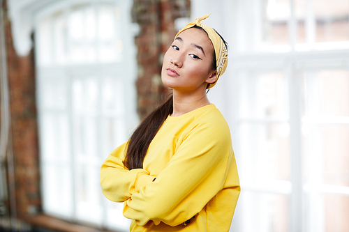 Young Asian or mix-raced woman in yellow sweatshirt and headband looking at you