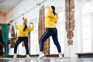 Young dancer in activewear training in front of large mirror in studio of modern dancing