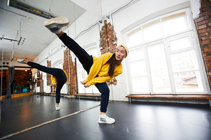 Young hip hop dancer in activewear stretching right leg while standing on the left one during training