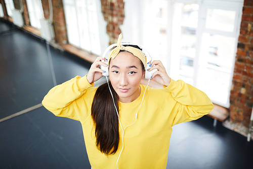 Young mixed-race woman in activewear putting on headphones before training in dancing studio