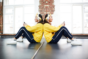 Active girl sitting by large mirror in studio of dancing and scrolling in smartphone at break