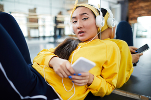Active girl with smartphone listening to music in headphones during break between trainings