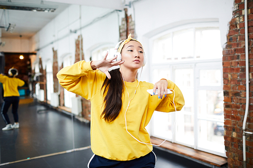 Girl in activewear listening to music in headphones and training in studio of modern dance