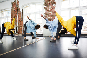 Two active girls exercising on the floor in front of large mirror during lesson of street dancing