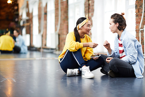 Young trainer consulting her learner at break between trainings while resting on the floor in studio