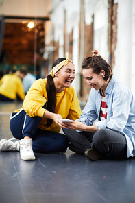 One of young breakdance performers showing something very funny to her friend in smartphone