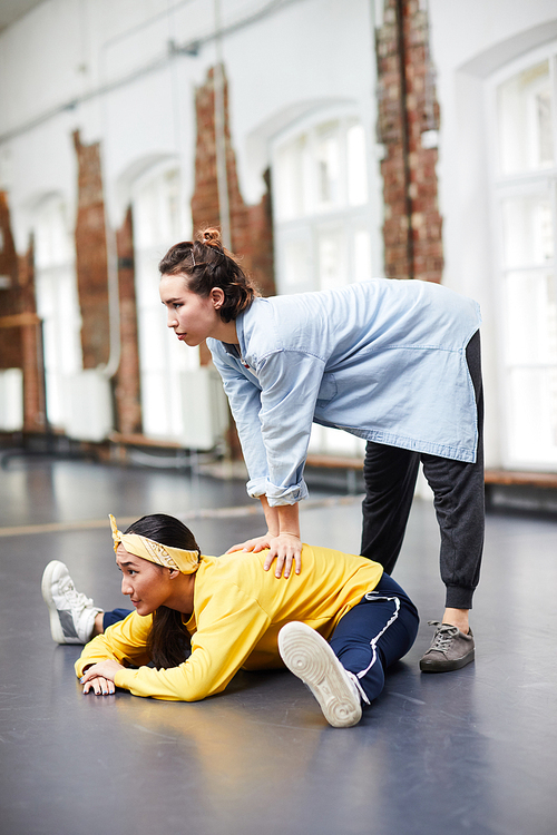 Young trainer helping girl with stretching exercise during training in modern dance studio