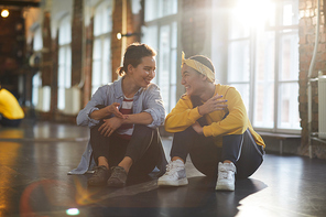 Two cheerful friendly girls sitting on the floor after training and discussing some training stuff