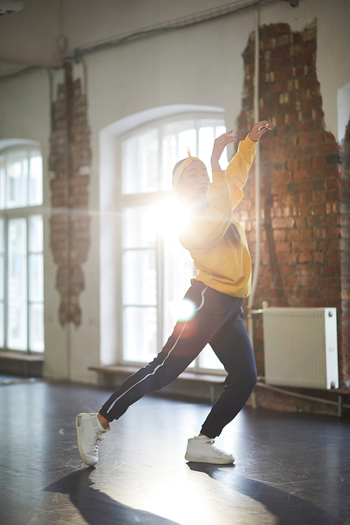Active girl in sweatshirt, sweatpants and cross-shoes performing breakdance in studio