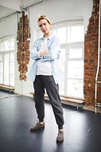 Young serious cross-armed active woman standing in studio of modern dance