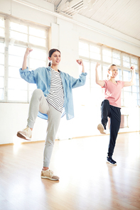 Two young dancers lifting one leg and arms while repeating move after trainer during workout in gym