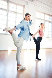 Young women in activewear repeating dance exercise after coach while training in studio