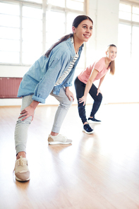 Two young women doing exercise for legs while training with coach in studio of dance or gym