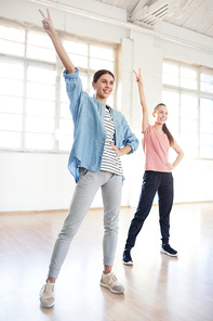 Happy young active females raising hands while repeating after coach in studio of modern dancing
