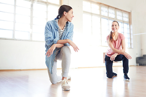 Two friendly girls standing on one knee on the floor of studio and discussing new exercise during training