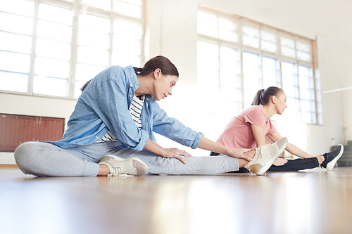 Young performers in activewear doing stretching exercise on the floor during class in modern studio