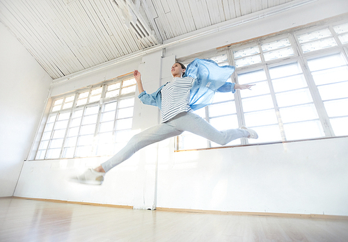 Energetic breakdancer in activewear leaping over floor of modern studio during workout
